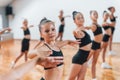 Standing and doing synchronised moves. Group of female kids practicing athletic exercises together indoors