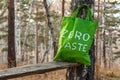 Standing in a forest on a bench near a birch, a textile green bag with the inscription zero waste.