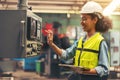 Standing in front of a control panel, a female industrial electrical engineer with a safety hardhat on her head and a tablet in