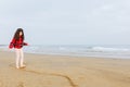 standing girl with long curly hair in red jumper and leggings playing on sand beach Royalty Free Stock Photo