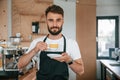 Standing and holding cup. Cafe worker in white shirt and black apron is indoors Royalty Free Stock Photo