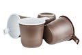 Standing, lying and upside down four unused disposable white plastic mugs with brown satin texture on the outside isolated on whit