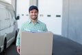 Standing man holding large cardboard box at warehouse loading dock, with paperwork and van Royalty Free Stock Photo