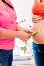 Standing pregnant women and midwife measuring circumference of b