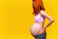 Standing red hair pregnant woman, on yellow background.