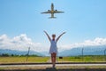 Standing on the road and stretching her hands in the sky to the plane one girl