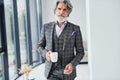 Standing in the room. Senior stylish modern man with grey hair and beard indoors