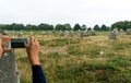 Standing stone alignments in Carnac with female tourist taking photos with cell phone selective focus