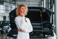 Standing and talking by phone. Woman with curly blonde hair is in autosalon
