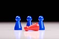 Standing three blue game pieces as winner and lying red figurine as loser on white table top with black background - Space for Royalty Free Stock Photo