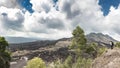 Standing tourist on a hill and looks black lava rocks and dramatic cloudy sky. Panoramic view of the slopes of the Batur volcano Royalty Free Stock Photo