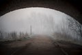 Standing under dark arched old bridge on creepy eerie footpath with fog and mist surrounding. Spooky atmosphere all alone.