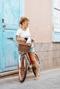 Standing woman in outdoor leisure activity ride a bike outside the blue door of her house in the street. Spring active healthy Royalty Free Stock Photo