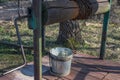 Standing on wooden door of well metal bucket attached to hoops frame and fixed by handle to chain wound on log wheel and axle