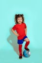 Photo of standing young soccer player girl 5-6 years holding football with foot on blue background, studio shot Royalty Free Stock Photo