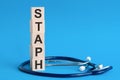 Staph word written on wooden blocks and stethoscope on light blue background Royalty Free Stock Photo