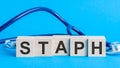 Staph word written on wooden blocks and stethoscope on light blue background