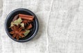 Star anise, bay leaf, black cardamom, and cinnamon stick in a gray bowl, left, top view, white background