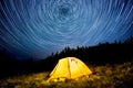Star circles above the night mountain forest and a glowing camping tent