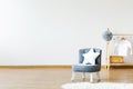 Star shaped white pillow placed on small armchair standing in white baby room interior with grey pompom and white shirt on wooden Royalty Free Stock Photo
