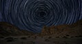 Star trails form circular patterns in a clear night sky above a rugged desert landscape. Royalty Free Stock Photo