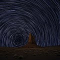 Star trails form circular patterns in the night sky above a towering rock formation in a Royalty Free Stock Photo