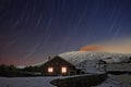 Star trails on Galvarina Refuge with windows glowing under snowy Etna Volcano