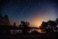 Star trails over the night lake. Beautiful night landscape with star trail above lake.  Scenic night view of the lake Royalty Free Stock Photo