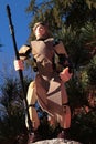 Star Wars LEGO action figure of Rey Skywalker in desert outfit with pole, standing on guard on rock with trees in background.