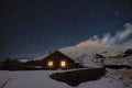 Starry night on Galvarina Refuge with windows glowing under snowy Etna Volcano