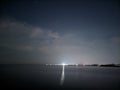 starry night sky on the edge of town with the reflection of lights in the calm sea water Royalty Free Stock Photo