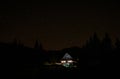 Starry night sky spans above a cottage in the middle of forest with lights on Royalty Free Stock Photo
