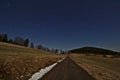 Starry night sky with star trails rotating around the North Star above a single lane road leading through fields Royalty Free Stock Photo