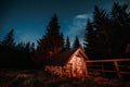 Starry sky with Milky Way and snow covered hut. Rustic old wooden hut in the forest - mountain shelter. Royalty Free Stock Photo
