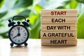 Start each day with a grateful heart text on wooden blocks with alarm clock and nature background. Motivational concept