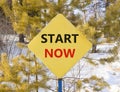 Start now symbol. Concept words Start now on beautiful yellow road sign. Beautiful forest snow blue sky background. Business Royalty Free Stock Photo