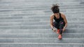 Muscular african american woman in sportswear, with modern headphones, fitness tracker, tying laces on sneakers on