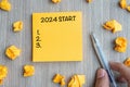 2024 Start word on yellow note with Businessman holding pen and crumbled paper on wooden table background. New Year, Resolutions, Royalty Free Stock Photo