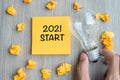 2021 Start words on yellow note and crumbled paper with Businessman holding lightbulb on wooden table background. New Year New