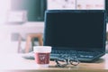 Start work with a take away cup of hot coffee that it have the word `wake up` with eyeglasses and laptop on table in office.