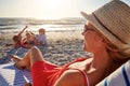 Starting the holidays stress-free. a woman lying on a lounger at the beach with her family in the background.