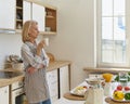 Thoughtful senior woman starting new day with coffee while standing in kitchen at home Royalty Free Stock Photo