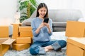 Startup small business, A young Asian woman checking online order on smartphone and packing boxes for products. Royalty Free Stock Photo