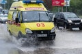 State Emergency Ambulance Reanimation Medical vehicle driving to help patient on city street road over deep muddy puddle, splashin