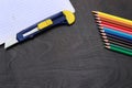 Stationery items on a dark table. Colored pencils, a notebook and a stationery knife in the composition Royalty Free Stock Photo