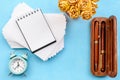 Stationery layout on a blue background. Alarm clock, white postcards, flowers and a smartphone.