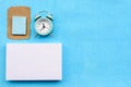 Stationery layout on a blue background, a stack of white cards, an alarm clock and a torn piece of kraft paper.