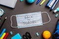 Stationery school supplies around the medical mask on black background. Top view. Concept of back to school
