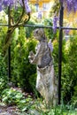 Statue with amphora in garden under pergola with wisteria in blooming spring garden