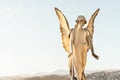 Statue of angel with wings against light sky at cemetery. Closing stoned angel in an old cemetery.. Graveyard old weathered stone Royalty Free Stock Photo